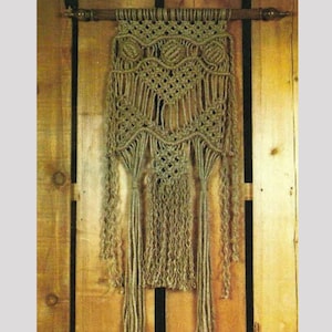 May include: A macrame wall hanging in shades of beige and tan, featuring intricate knotting patterns. The piece is suspended from a wooden rod and has long, fringed tassels. The design includes diamond and floral motifs, creating a textured, bohemian aesthetic.