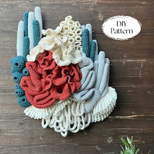 May include: A handmade crochet wall hanging resembling coral. It features a variety of textures and colours, including teal, cream, red, and grey. The text "DIY Pattern" is in a white oval on the right. The artwork is mounted on a wooden background.