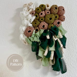 Op de afbeelding: Textiel wandkunst met gehaakte cirkels in bruin en olijfgroen, en witte, lichtgroene en donkergroene stoffen accenten. Het kunstwerk heeft een DIY patroon label.