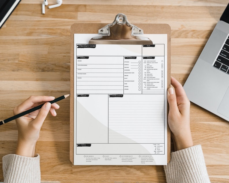 May include: A white clipboard with a black checklist and a project name section. The clipboard is on a wooden surface with a laptop and a pair of earbuds.
