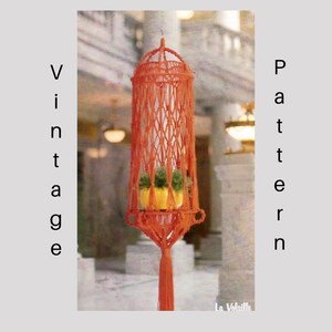 May include: A vintage macrame plant hanger with a bright orange cord and a small potted plant inside. The hanger is hanging from the ceiling in a room with a light brown tiled floor.