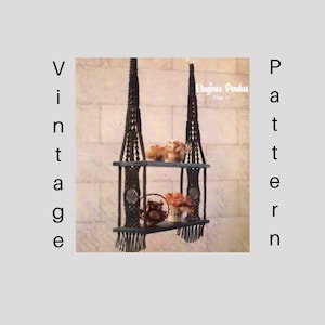 May include: A dark brown macrame plant hanger with two shelves, displaying decorative flowers. The image includes the text "Vintage Pattern" and "Etagères Pendus Page 11".