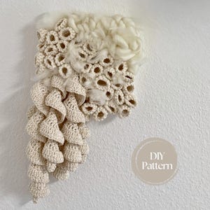 Può includere: Applique da parete fatto a mano color crema con un design strutturato. L'opera d'arte presenta una combinazione di elementi tessuti, all'uncinetto e soffici, creando un'estetica unica e organica. Montato su una parete bianca.