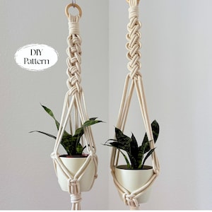 May include: Two macrame plant hangers with cream-colored rope, each holding a white ceramic pot with a green plant. The hangers are suspended from wooden rings. The image includes the text "DIY Pattern".