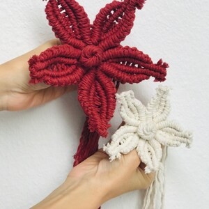 Puede incluir: Dos adornos de estrellas de macram&eacute;, uno rojo y otro blanco, con largas borlas que cuelgan de la parte inferior.