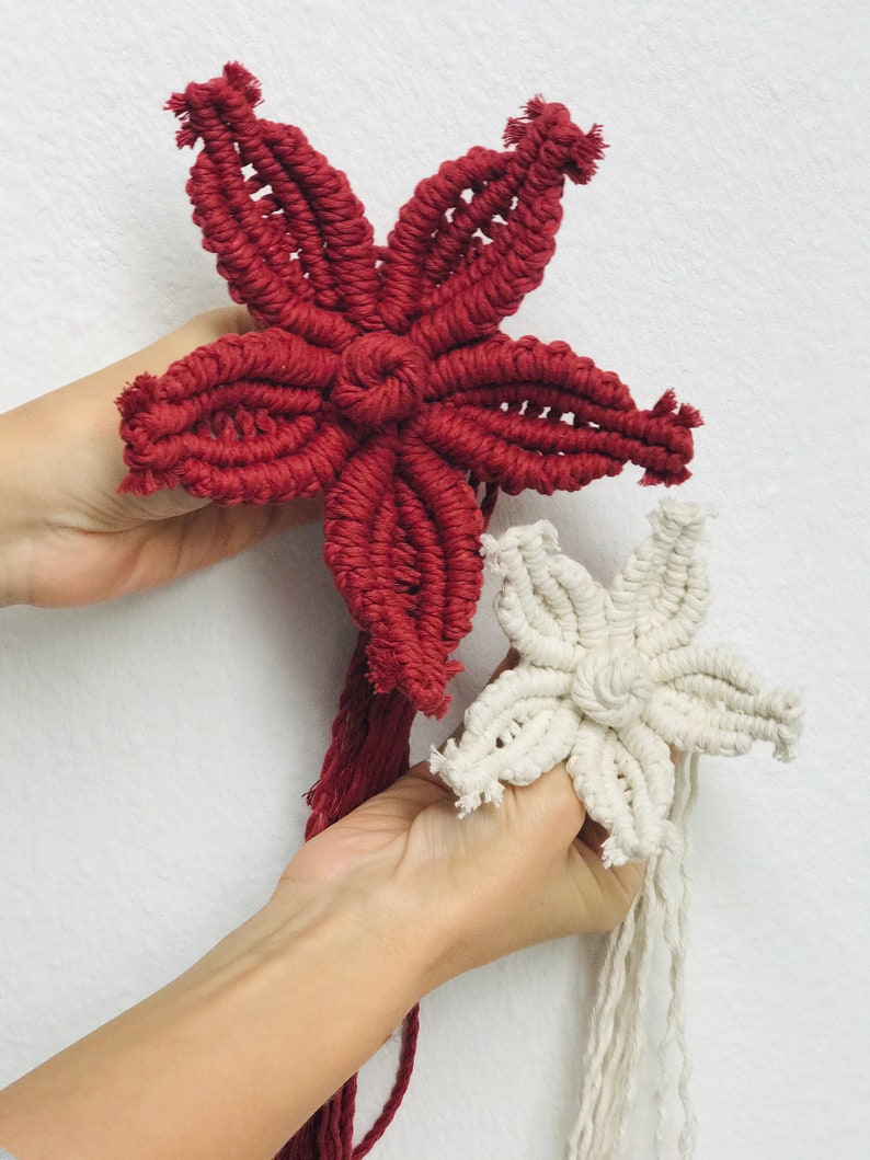 Puede incluir: Dos adornos de estrellas de macram&eacute;, uno rojo y otro blanco, con largas borlas que cuelgan de la parte inferior.