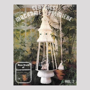 Puede incluir: Un libro de patrones de macramé para colgar plantas vintage, "Classics Macrame Plantiere", volumen 2, con un macramé blanco para colgar plantas con cuentas verdes colgando en un invernadero.