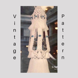 Può includere: Una lampada a sospensione in macramé bianca con perline blu e una frangia a nappe. La lampada è appesa in una porta con una cornice in legno.