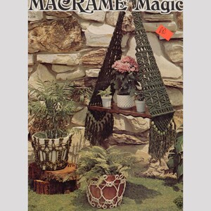 Puede incluir: Un colgador de plantas de macramé verde con un estante de madera y tres plantas en macetas. El colgador está colgado de una pared de piedra. El texto "MACRAME Magic" es visible en la parte superior de la imagen.