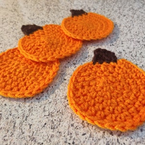 Pode incluir: Quatro  tapetes de crochê de abóbora laranja com hastes marrons. Os tapetes estão empilhados uns sobre os outros.