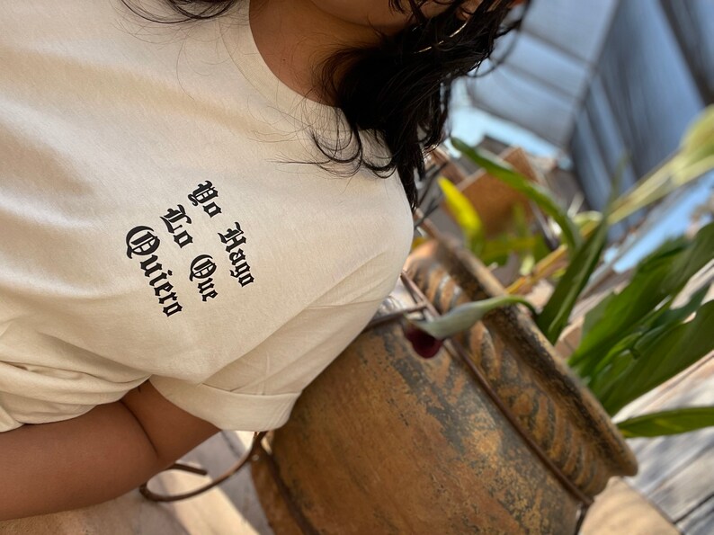May include: A white t-shirt with black text that reads "Yo Hago Lo Que Quiero" in a gothic font.