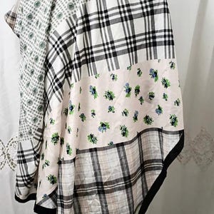 May include: A patchwork scarf with various patterns. The scarf features sections of black and white plaid, floral prints, and a green and white floral design. The edges are trimmed with a black border. The scarf is draped over an unseen object.