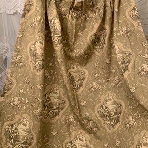 May include: Olive green curtain panel with a repeating toile pattern featuring scenes of people in a landscape. The fabric has a floral and scroll design in cream and brown. The curtain is gathered at the top.