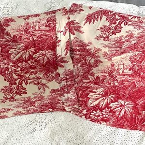 May include: Two rectangular fabric panels featuring a red and cream toile de jouy pattern. The design displays intricate illustrations of dense foliage, trees, and architectural structures printed in a deep red ink on a light cream background.
