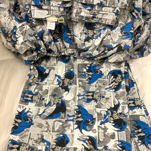May include: A two-piece Batman pajama set. The pajamas feature a repeating comic book panel design with Batman in action poses, in shades of blue, black, gray, and white. The top has a collar and pockets. The bottom is a skirt.