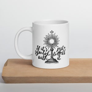 Op de afbeelding: Witte keramische mok met een zwart-wit afbeelding van een religieus symbool en de tekst "If it's just a symbol, to hell with it."  Flannery O'Connor.