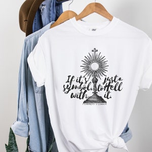 Op de afbeelding: Wit T-shirt met een zwarte afbeelding van een religieus symbool en de tekst "If it's just a symbol, to hell with it."  Flannery O'Connor.