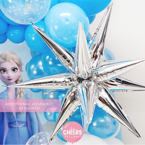 May include: A silver star-shaped balloon with pointed tips, surrounded by blue balloons. The text "ADDITIONAL ASSEMBLY REQUIRED" is visible in pink on a white background. The text "CHEERS BALLOONS" is visible in pink on a white background.