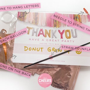 May include: A kit for creating a 'Thank You' balloon banner. The kit includes gold, pink, and silver foil balloons, a straw for inflating, a needle for stringing, and fishing line for hanging. The kit also includes instructions on the back.