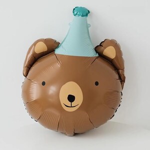 May include: A brown bear balloon with a blue party hat. The balloon has a simple, cartoon-like face with black eyes and a brown nose.