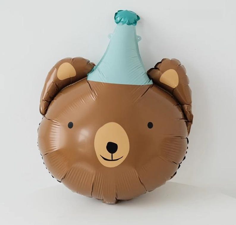 May include: A brown bear balloon with a blue party hat. The balloon has a simple, cartoon-like face with black eyes and a brown nose.