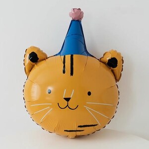May include: A yellow tiger face balloon with a blue party hat and a pink flower on top. The balloon has black stripes and a cute cartoon face.