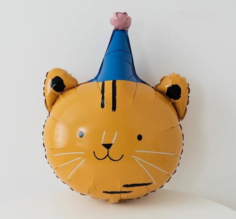 May include: A yellow tiger face balloon with a blue party hat and a pink flower on top. The balloon has black stripes and a cute cartoon face.