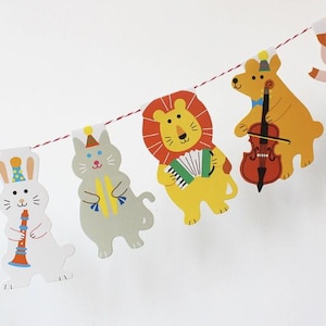 以下が含まれることがあります： 動物のキャラクターが楽器を演奏しているカラフルなガーランド。白いウサギはクラリネットを、灰色の猫はタンバリンを、黄色のライオンはアコーディオンを、茶色のクマはチェロを、白い鳥はトランペットを演奏しています。