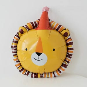 May include: A yellow lion balloon with a red and white party hat. The balloon has brown and orange stripes around the edge.