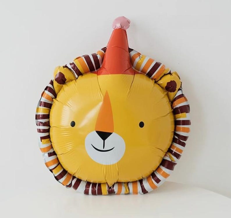 May include: A yellow lion balloon with a red and white party hat. The balloon has brown and orange stripes around the edge.