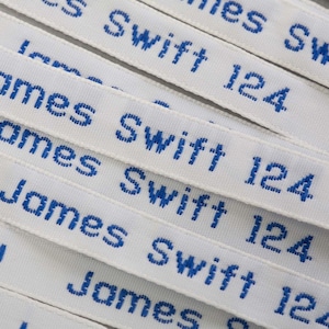 May include: Close-up of multiple white fabric labels with blue embroidered text. The text reads "James Swift 124".