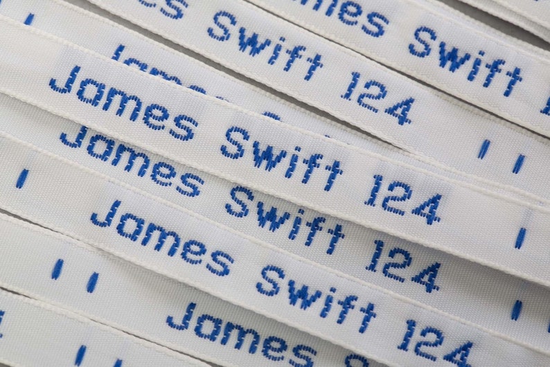 May include: Close-up of multiple white fabric labels with blue embroidered text. The text reads "James Swift 124".