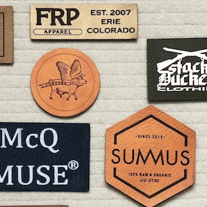 May include: A selection of leather patches with different designs and text. The patches feature a rooster, a tiger, a pig, a bull, an elephant, a gun, and text that reads "ROOSTERS BREWING CO.", "FRP APPAREL", "McQ MUSE", "STACK BUCKETS CLOTHING", "COWTOWN MCMXCVI", "Alfil Walhikma", and "SUMUS 100% RAW & ORGANIC JIU JITSU".
