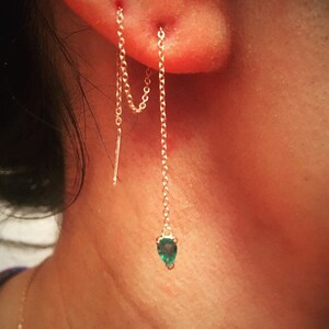 May include: A gold chain earring with a teardrop-shaped emerald green gemstone hanging from the bottom.