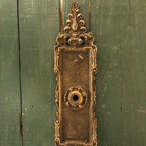 May include: Ornate gold-toned metal door knocker with a keyhole and intricate scrollwork design.