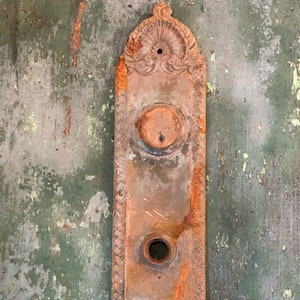 May include: An antique, ornate, metal door plate with two round openings. The plate is rusty and has a green patina.