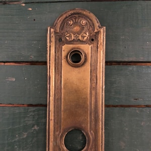May include: Antique brass door plate with ornate floral designs and two keyhole openings.