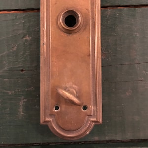 May include: A vintage brass door knob with a decorative design and a keyhole. The knob is attached to a rectangular plate with a rounded top.