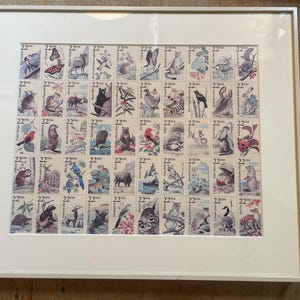 May include: Framed collection of vintage 22-cent USA stamps featuring various animals, including a butterfly, bear, and deer. The stamps are arranged in a grid pattern within a white mat and frame, creating a decorative piece.