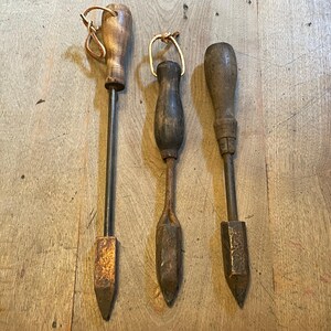 May include: Three antique soldering irons with wooden handles and metal tips. The tips are pointed and the handles are worn with age.