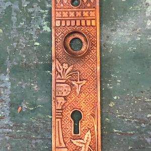 May include: Antique brass door plate with an ornate design featuring a keyhole, a circular opening, and floral motifs.