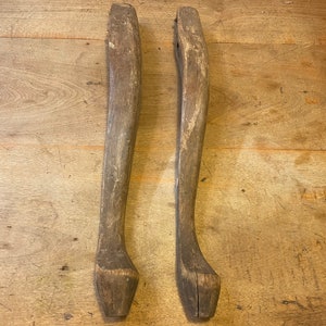 May include: Two wooden chair legs, each with a curved shape at the bottom. The legs are made of dark brown wood and have a rough, unfinished texture.