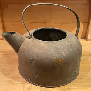 May include: A vintage copper kettle with a worn patina. The kettle has a handle and a spout. It is a rustic and antique kitchen item.