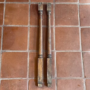 May include: Two wooden balusters with a simple turned design. The balusters are brown and have a worn finish.