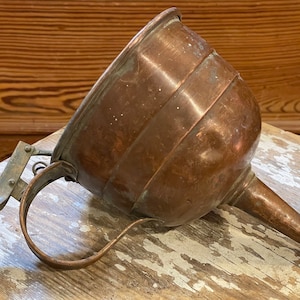 May include: A vintage copper funnel with a long spout and a handle. The funnel has a worn, aged patina and is made of thick copper.