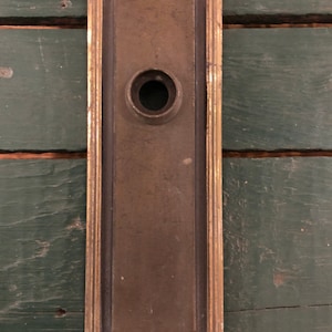 May include: A vintage brass door plate with a keyhole and a decorative border. The plate is rectangular and has a worn, aged look.