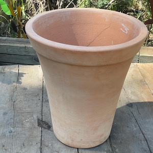 May include: A large, unglazed terracotta flower pot with a wide rim and a tapered body. The pot has a natural, earthy color and a slightly rough texture. The pot is sitting on a weathered wooden surface.