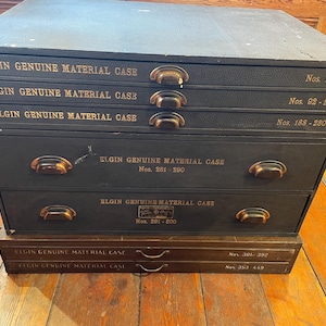 May include: A black wooden box with six drawers labeled "Elgin Genuine Material Case" and numbered 1-91, 92-187, 188-280, 281-290, 201-200, 301-392, and 393-449.