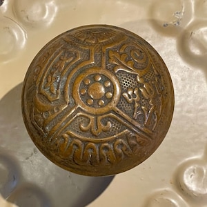 May include: A vintage brass door knob with an intricate design featuring a central rosette and four radiating arms with floral motifs.