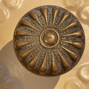May include: A brass door knob with a decorative design of a sunburst with a central circle. The knob has a worn, aged finish.